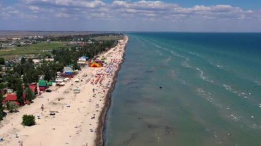 Yazın sahilde güzel bir uçuş. İnsanlar deniz kenarında dinleniyor. Turistler için evler. Plaj şemsiyeleri, gezintiler, denizde yüzen insanlar..