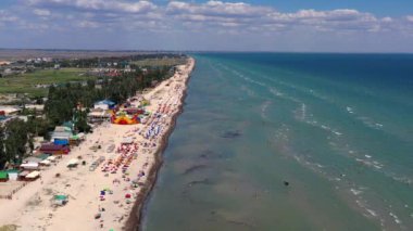 Yazın sahilde güzel bir uçuş. İnsanlar deniz kenarında dinleniyor. Turistler için evler. Plaj şemsiyeleri, gezintiler, denizde yüzen insanlar..