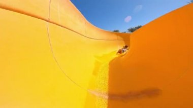 Küçük bir çocuk sarı bir su kaydırağından aşağı iniyor ve mavi bir havuza düşüyor. Su çekimleri. Yüksek hız.