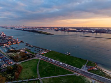 Sahil kenarındaki deniz feneri, botlar, yeşil park ve marina binaları deniz altyapısını manzaralı cazibeyle harmanlarken nehir kıyısı vinçleri ve sanayi rıhtımlarının hava günbatımı manzarası uzak kıyılara uzanır..