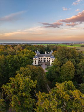 Ormanlık alanlarda ve açık alanlarda bacaları olan tarihi malikâne simetrik tasarımı, sonbahar renkleri ve sıcak gökyüzü tonlarıyla sakin, pitoresk bir kırsal manzara oluşturur..