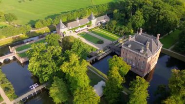 Çevrelenmiş hendek adasındaki tarihi bir şatonun havadan görünüşü, resmi bahçeler, emlak binaları ve yeşil tarlalar, su yolları ve resimli kırsal bir manzara arasında yer alan yakınlardaki bir kasaba..