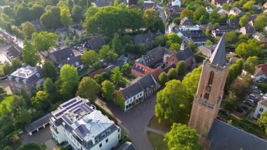Kırmızı kiremitli çatıları, yemyeşil yeşillikleri ve merkezinde uzun bir kilise kulesi olan büyüleyici bir Avrupa kasabasının havadan görünüşü. Dar sokaklar ve rahat evler huzurlu, resimli bir manzara yaratır..