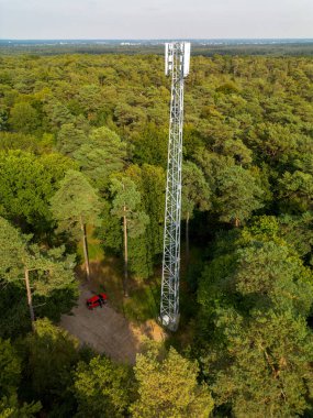 Uzun bir telekom kulesi ve toprak erişim yolu olan sık ormanın havadan görünüşü teknoloji ve doğal manzaranın kesişimini vurguluyor..