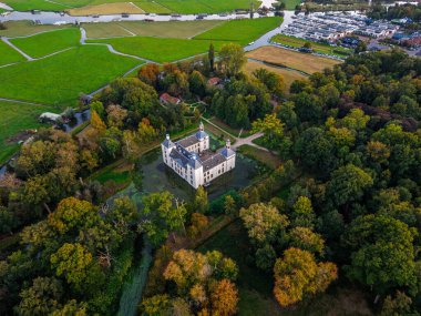 Ormanlık alanlarda ve açık alanlarda bacaları olan tarihi malikâne simetrik tasarımı, sonbahar renkleri ve sıcak gökyüzü tonlarıyla sakin, pitoresk bir kırsal manzara oluşturur..