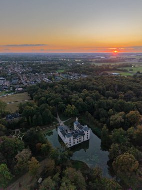 Günbatımında hava manzarası, hendek ve kuleleri olan, sık ormanlara yuva yapmış bir bina gibi, dolambaçlı yollar girişe götürür, yakınlardaki kasaba üzerinde sıcak gökyüzü parıldar, tarihi, doğayı ve modern yaşamı harmanlar.
