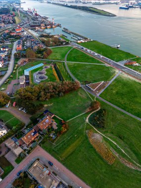 Araçlar, kırmızı bisiklet yolu, dairesel gözcü, geometrik yeşil alanlar, tenis kortları ve orman ve kıyı şeridi tarafından çerçevelenmiş yoğun yerleşim alanları ile kıyı kentsel bölge yolu hava görüntüsü.