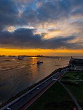 Endüstriyel deniz manzaralı gemi yaprakları, vinçler ve liman yapıları dramatik bulutlara karşı siluet oluştururken altın su üzerinde uyanır.