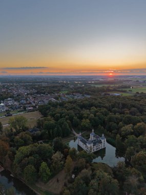 Günbatımında hava manzarası, hendek ve kuleleri olan, sık ormanlara yuva yapmış bir bina gibi, dolambaçlı yollar girişe götürür, yakınlardaki kasaba üzerinde sıcak gökyüzü parıldar, tarihi, doğayı ve modern yaşamı harmanlar.