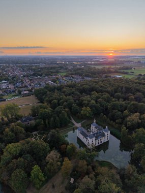 Günbatımında hava manzarası, hendek ve kuleleri olan, sık ormanlara yuva yapmış bir bina gibi, dolambaçlı yollar girişe götürür, yakınlardaki kasaba üzerinde sıcak gökyüzü parıldar, tarihi, doğayı ve modern yaşamı harmanlar.