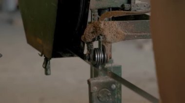 Dikey bıçak ve metal tekerlekleri olan tozlu testere kılavuz sisteminin yakın çekimi, yeşil çerçeve atölye ayarlarında aktif kullanım öneriyor.