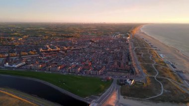 Kırmızı çatıları, kıvrımlı sahil yolları, kanalı ve deniz ve kum tepeleri üzerindeki altın ışıklarıyla kıyı şehrinin hava günbatımı manzarası..