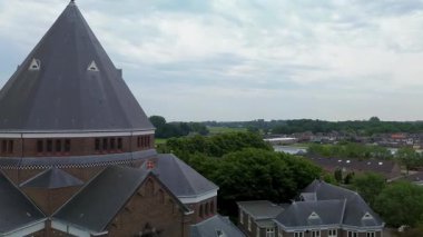 Konik çatısı olan tarihi tuğla kilise, Gotik pencereler ve çevresi yeşillik, ek bina ve banliyö evleriyle çevrili çan kulesi..