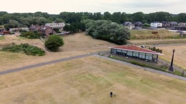 Yeşil çatılı modern bina, siyah anıt ve kale 1881 tarihsel ve doğal çevreyle çağdaş tasarımı harmanlayan işaret levhası ile yarı kırsal kasaba havası..