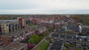 Kentsel konut manzarası düz çatıları ve balkonları olan kırmızı tuğlalı daireler fayanslı evler ve bulutlu gökyüzü altında yeşil alanlar ile harmanlanmış..