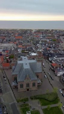 Sahil kasabasının tarihi kilisesinin havadan görünüşü. Saat kulesi kızıl çatılar arasında yükseliyor. Ve bulutlu gökyüzü altında denize yakın modern bloklar..