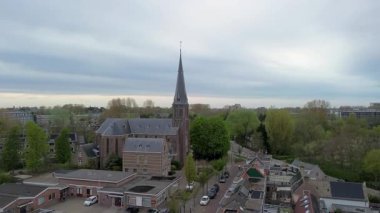 Çan kulesi ve haçı olan Hollanda kasabası gotik kilisesi evleri, ağaçları ve sisli banliyö zeminiyle çevrili..