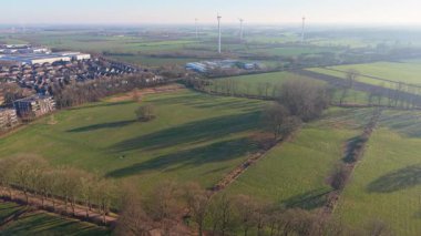 Hollanda kırsalının hava manzaralı köşegen yolu uzun gölgeler, yeşil tarlalar, dağınık evler ve uzak rüzgar türbinleri sakin, sürdürülebilir bir kırsal alan oluşturuyor..