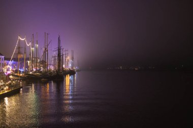 Gece vakti Hollanda liman gemileri sicim ışıklarıyla bezenmiş sisli suda yansımalar parıldıyor, deniz mirasıyla şenlikli atmosferi harmanlıyorlar..