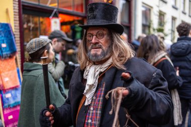 Deventer, Overijssel, Hollanda - 14.12.2025: Charles Dickens Festivali 'nde. Silindir şapkalı ve paltolu adam, festival sokak etkinliğinde baston ve iple Dickens karakterini canlandırıyor..