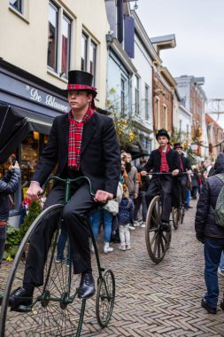 Deventer, Overijssel, Hollanda - 14.12.2025: Charles Dickens Festivali 'nde. Silindir şapkalı adamlar, canlı İngiliz temalı sokak geçit töreni sırasında eski motosikletlerle festival mağazalarının önünden geçiyorlar..