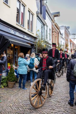 Deventer, Overijssel, Hollanda - 14.12.2025: Charles Dickens Festivali 'nde. Silindir şapkalı adamlar, canlı İngiliz temalı sokak geçit töreni sırasında eski motosikletlerle festival mağazalarının önünden geçiyorlar..