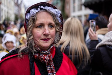 Deventer, Overijssel, Hollanda - 14.12.2025: Charles Dickens Festivali 'nde. Kırmızı pelerinli ve dantelli kadın, Victoria temalı sokak kutlaması için giyinmiş, şenlikli kalabalığın içinde duruyor..