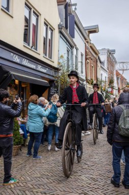 Deventer, Overijssel, Hollanda - 14.12.2025: Charles Dickens Festivali 'nde. Silindir şapkalı adamlar, canlı İngiliz temalı sokak geçit töreni sırasında eski motosikletlerle festival mağazalarının önünden geçiyorlar..
