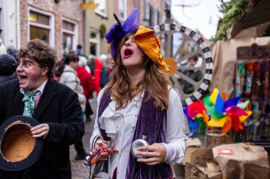 Deventer, Overijssel, Hollanda - 14.12.2025: Charles Dickens Festivali 'nde. Şenlik şapkalı iki tiyatro figürü dönen tekerlek ve renkli market tezgahının yanında gösteri yapıyorlar..