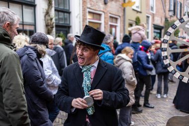 Deventer, Overijssel, Hollanda - 14.12.2025: Charles Dickens Festivali 'nde. Şenlik pazarında pembe yelek içindeki etkileyici gençler tiyatro kalabalığı ve renkli tezgahlarla şarkı söylüyor..