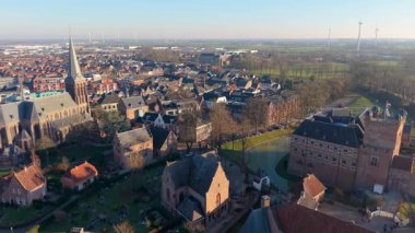 Hollanda şehrinin şatosu, hendeği, kilise kulesi, gengelli çatıları, düz alanları ve gelenek ve yenilikleri harmanlayan rüzgar türbinleri ile hava manzarası.