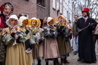 Deventer, Overijssel, Hollanda - 14.12.2025: Charles Dickens Festivali 'nde. 19. yüzyıldaki çocuklar, kırmızı şapkalı ve ceketli öğretmenlerinin yanında karatahta geçidi olan okul kostümleri..
