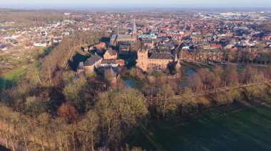 Kırmızı tuğladan kalesi, kilise kulesi, hendeği ve çevresindeki ormanın kentsel ve kırsal bölgelere karıştığı tarihi Avrupa kasabasının havadan görünüşü.