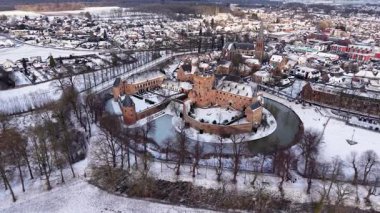 Kasabayı kırmızı tuğladan kale ve donmuş ortaçağ kuleleriyle kaplayan kar, yoğun konutlar ve sakin kış manzarasında kilise kulesiyle tezat oluşturuyor..