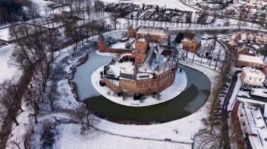 Kırmızı tuğladan kale ve donmuş ortaçağ kuleleriyle kaplı kar manzarası modern evlerle ve huzurlu kış manzarasındaki kilise kulesiyle tezat oluşturuyor..