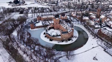 Kırmızı tuğladan kale ve donmuş ortaçağ kuleleriyle kaplı kar manzarası modern evlerle ve huzurlu kış manzarasındaki kilise kulesiyle tezat oluşturuyor..