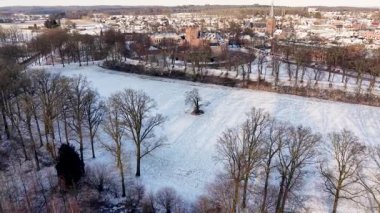 Dağınık yapraksız ağaçlarla kaplı kırsal alanların karlı hava manzarası. Orman ve kasabayla çevrili. Şato ve kilise kulesi..