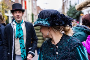Deventer, Overijssel, Hollanda - 14.12.2025: Charles Dickens Festivali 'nde. Şenlik caddesinde, üzerinde silindir şapka olan adamın yanında duran kadife ceketli ve dantel şapkalı kadın..