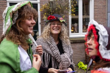 Deventer, Overijssel, Hollanda - 14.12.2025: Charles Dickens Festivali 'nde. Klasik başlık ve eşarplı üç kişi, tuğla binanın dışında şenlikli bir anın tadını çıkarıyorlar..