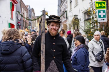 Deventer, Overijssel, Hollanda - 14.12.2025: Charles Dickens Festivali 'nde. Yığınla şapkalı ve eski moda ceketli bir adam, festivalsel sokak etkinliğinde merdiveni kalabalıkla ve Noel dekoruyla tutuyor..