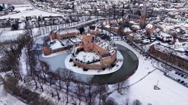 Kırmızı tuğladan kale ve donmuş ortaçağ kuleleriyle kaplı kar manzarası modern evlerle ve huzurlu kış manzarasındaki kilise kulesiyle tezat oluşturuyor..
