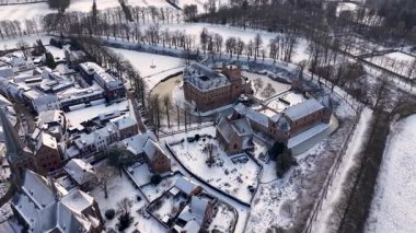 Kırmızı tuğladan kale ve donmuş ortaçağ kuleleriyle kaplı kar manzarası modern evlerle ve huzurlu kış manzarasındaki kilise kulesiyle tezat oluşturuyor..