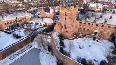 Kar, kuleleri, duvarları ve iç avluları olan kırmızı tuğladan kale kompleksi kış kasabasının çatıları, ağaçları ve çevreleyen binalar arasında durmaktadır..