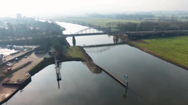 Bir köprü, kırsal bir alanda sakin bir nehri, tarlaları, ağaçları ve küçük bir nehir kenarı çalışma alanını kapsar ve açık bir altyapı ve doğa karışımı oluşturur..