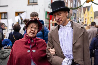 Deventer, Overijssel, Hollanda - 14.12.2025: Dönem kostümlü iki kişi, şenlikli bir halk etkinliği sırasında canlı bir sokakta birlikte duruyorlar.