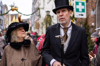 Deventer, Overijssel, Hollanda - 14.12.2025: Victoria dönemi kostümlü iki kişi, halka açık bir festival sırasında dekoratif bir sokakta yürüyor.