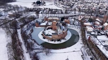 Karlı bir hendekle çevrili dairesel tuğla bir kalenin havadan görünüşü. Kış kasabasında evler, yollar, ağaçlar ve yakınlardaki büyük bir kilise..