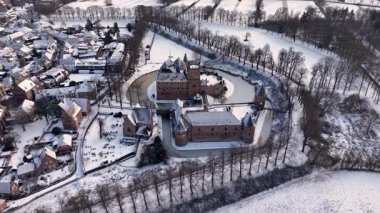 Önünde tuğla kale ve hendek bulunan, yoğun evler, kilise, açık araziler ve kış ağaçlarıyla çevrili, karla kaplı bir Avrupa kasabasının havadan görünüşü..