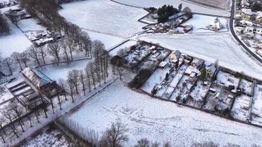 Dağınık evler, ağaçlık yollar, açık araziler ve sakin bir kırsal alan oluşturan sakin kış yolları ile kaplı bir kırsal alanın havadan görünüşü.
