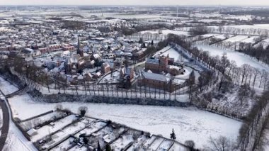 Merkezi kale ve hendekli bir kar manzarası, yakınlardaki bir kilise, yoğun konutlar, açık kış alanları ve uzak rüzgar türbinleri tarihi ve modern elementlerin bir karışımını oluşturuyor..